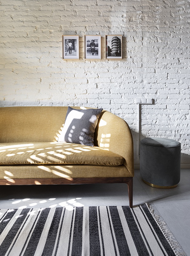 En el salón destaca un sofá con estructura de madera y tapizado en un color mostaza para dar calidez al mini piso del Ensanche