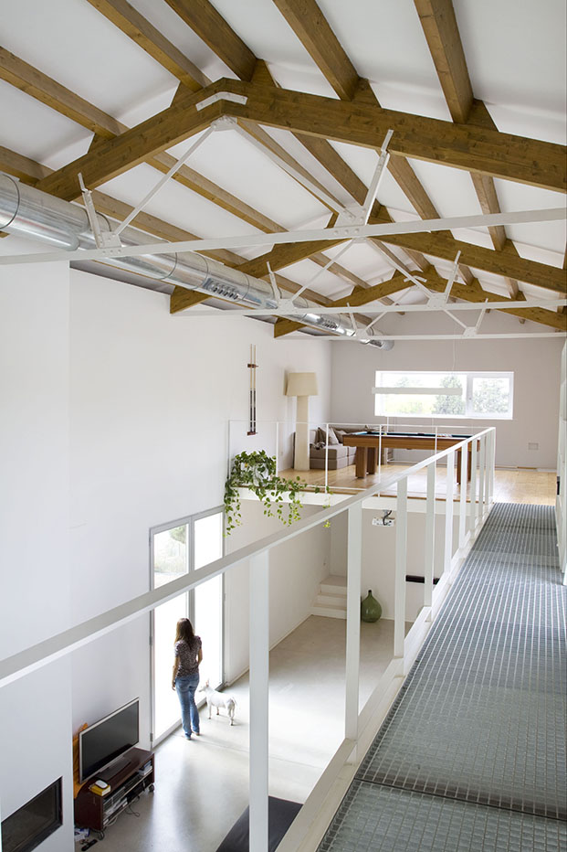 Una casa de campo rehabilitada por CÜ4 Arquitectura, con cerchas de madera y pasarela de metal.