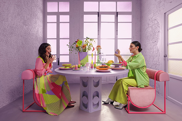 dos mujeres sentadas en sofás rosas y mesa violeta, vestido de colores de diseño