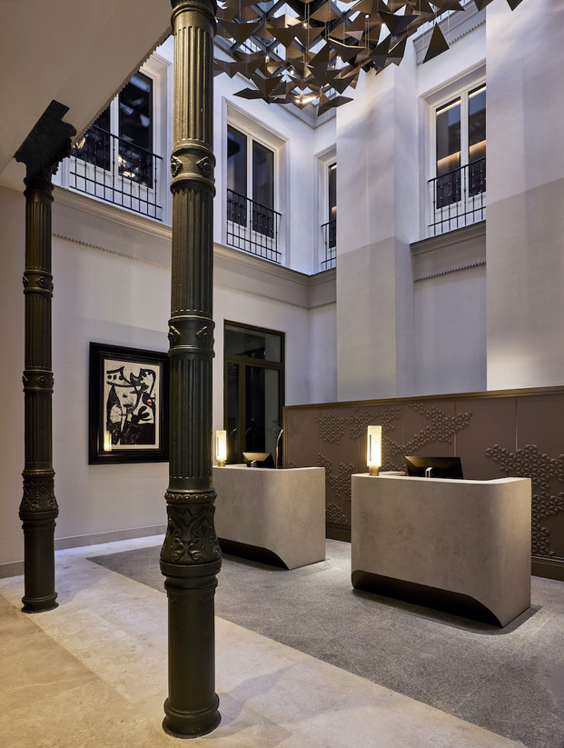 Recepción de hotel, columnas de metal, interiorismo en colores neutros, mostradores geométricos