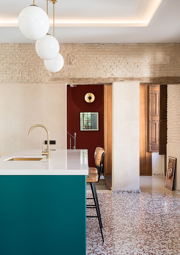pared de ladrillo visto en cocina, encimera blanca de isla con muebles de colores, suelo de terrazo